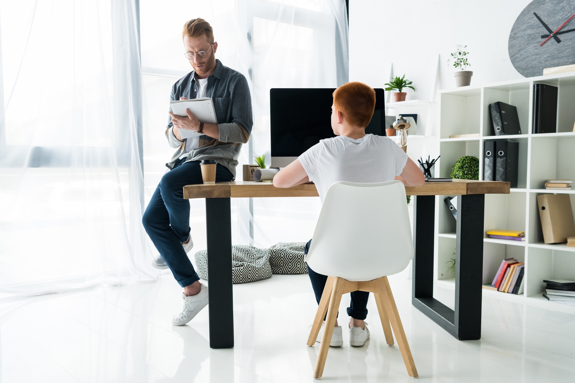 father writing to notebook, son using computer at home