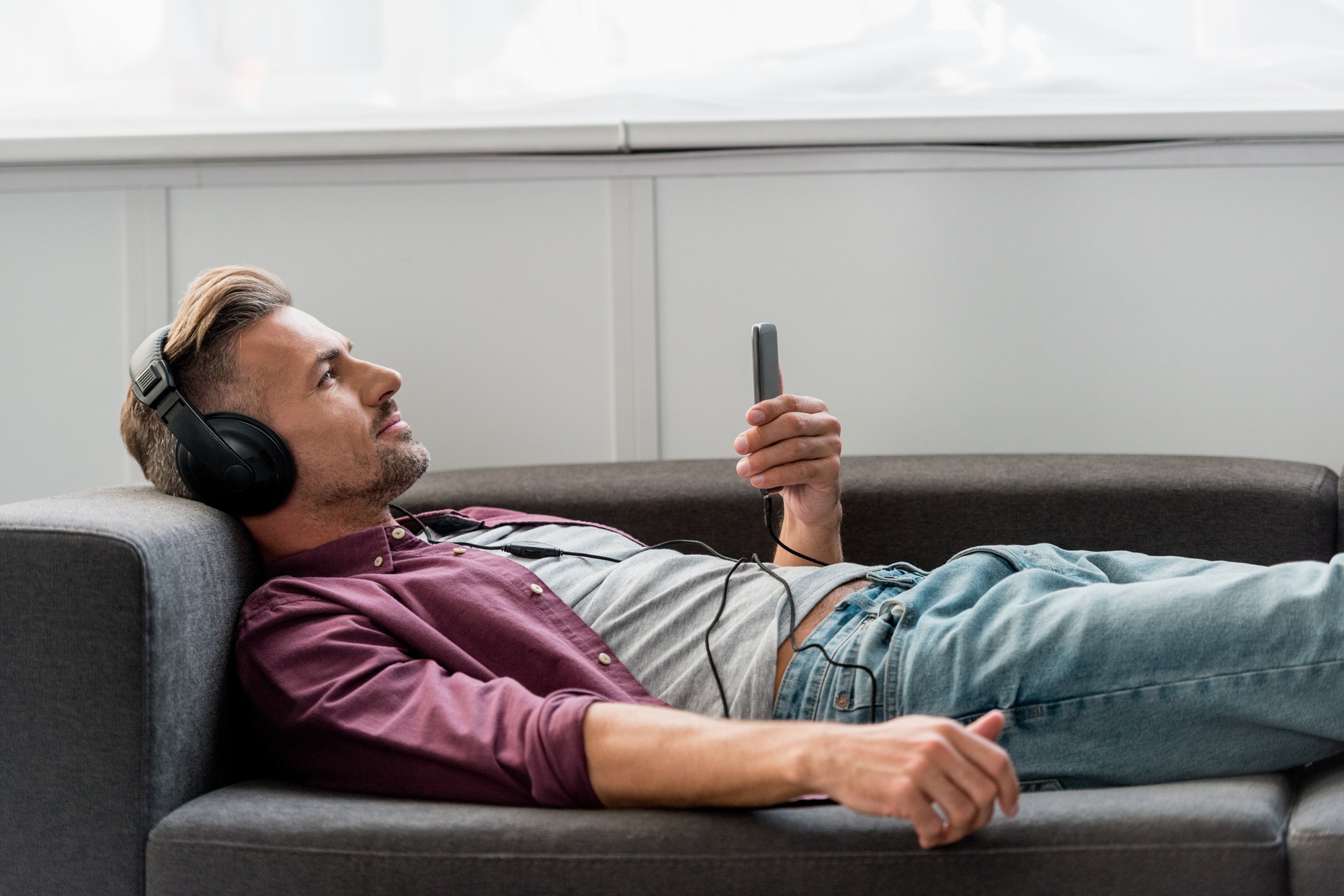 happy man with smartphone listening music while laying on sofa
