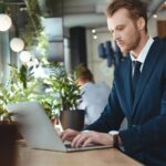 side view of focused businessman using laptop at table in cafe