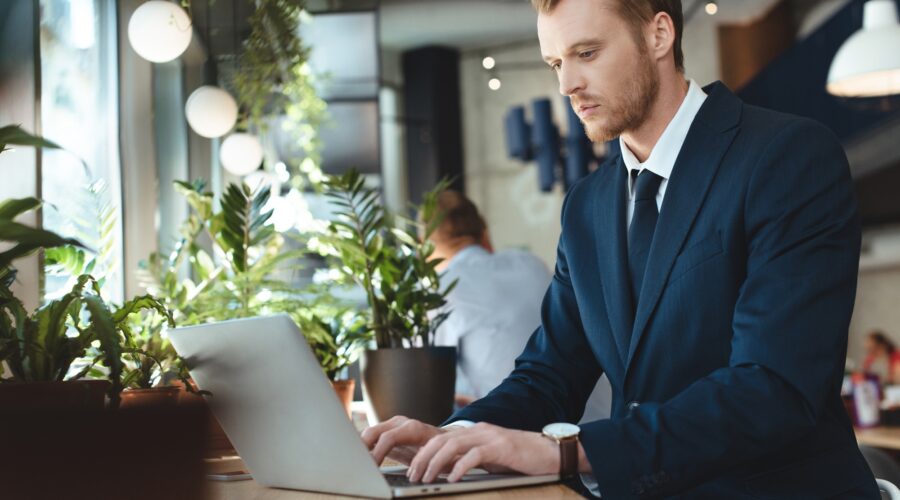 side view of focused businessman using laptop at table in cafe