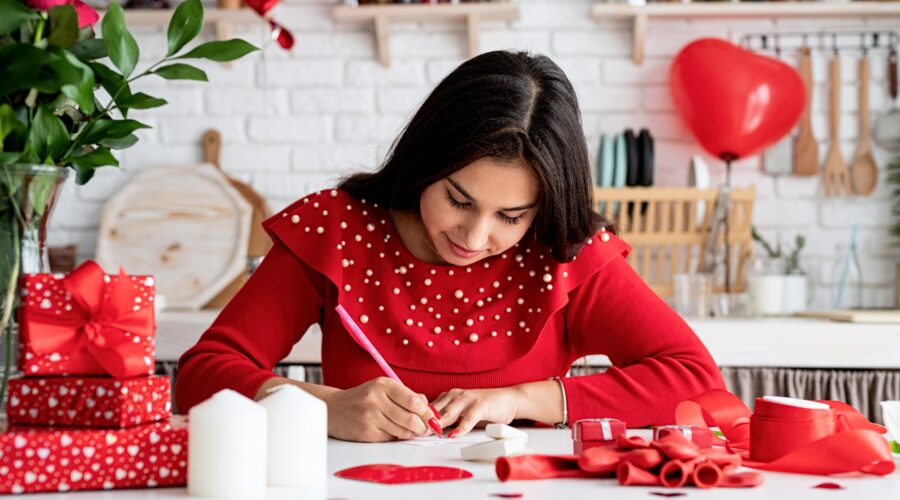Woman in red dress writing love letter sitting at the decorated kitchen