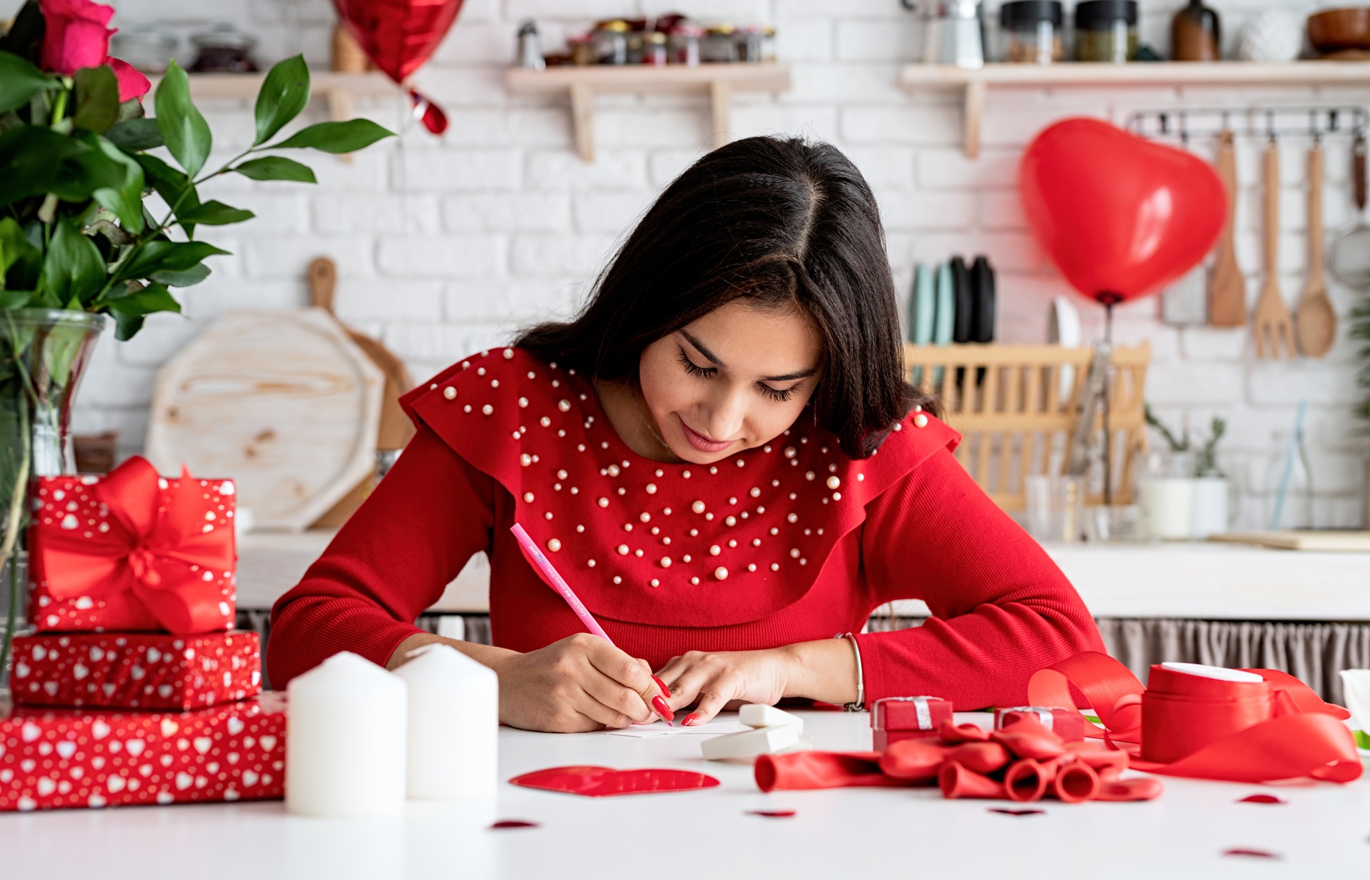 Woman in red dress writing love letter sitting at the decorated kitchen